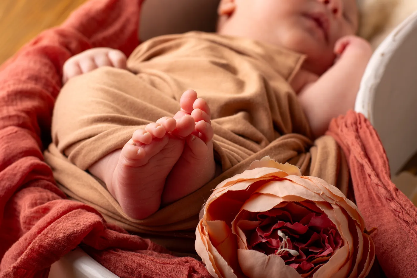 Kleine Babyfüße auf einer rostfarbenen Decke neben einer Blüte