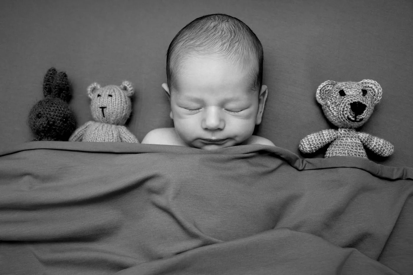 Schwarz-Weiß: Schlafendes Baby unter einer Decke zwischen gestrickten Kuscheltieren