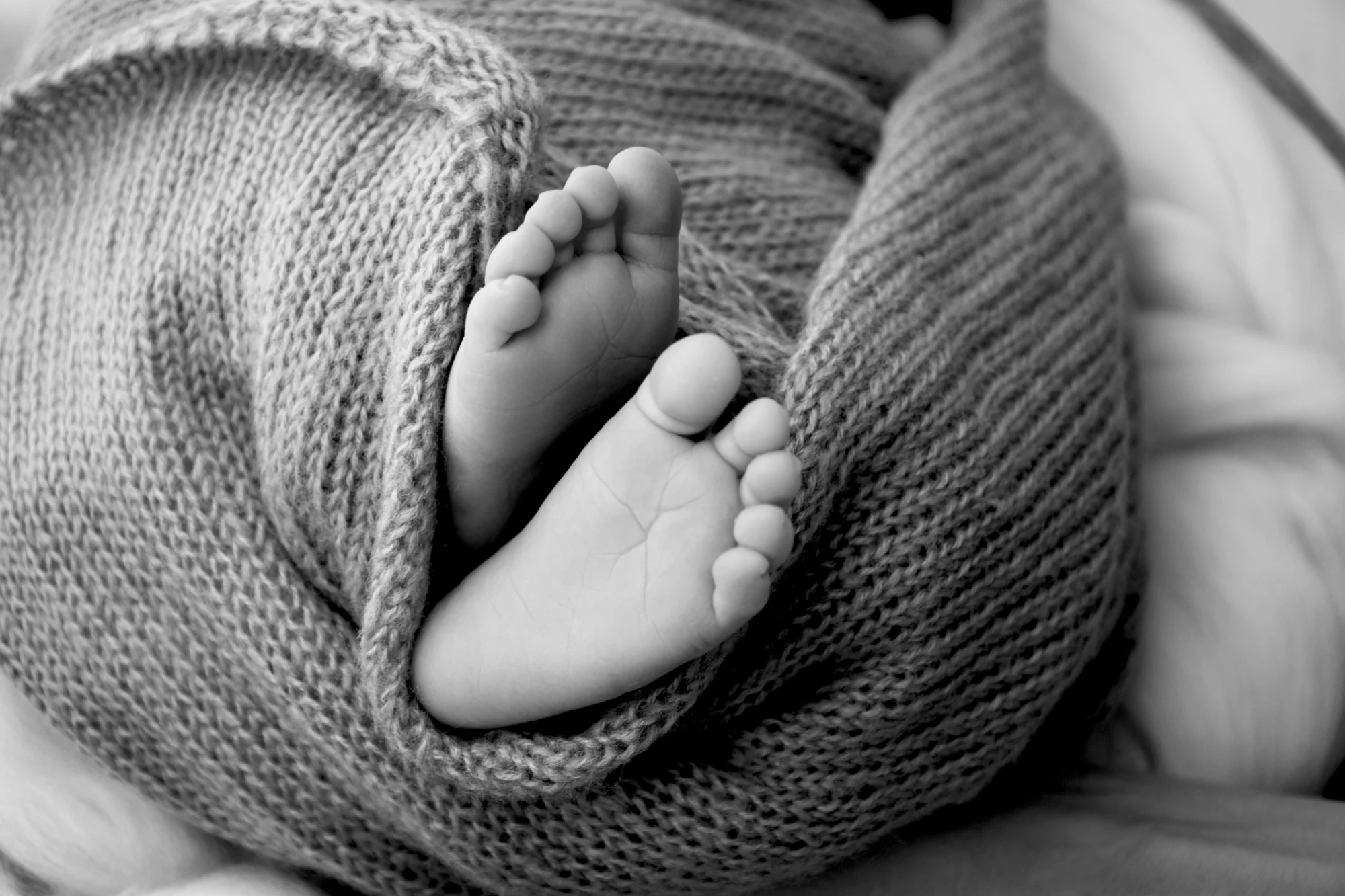 Schwarz-Weiß: Babyfüße schauen aus einer Strickdecke