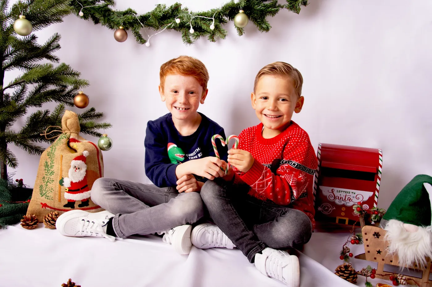 Zwei Jungen sitzen lachend mit Zuckerstangen vor weihnachtlicher Dekoration