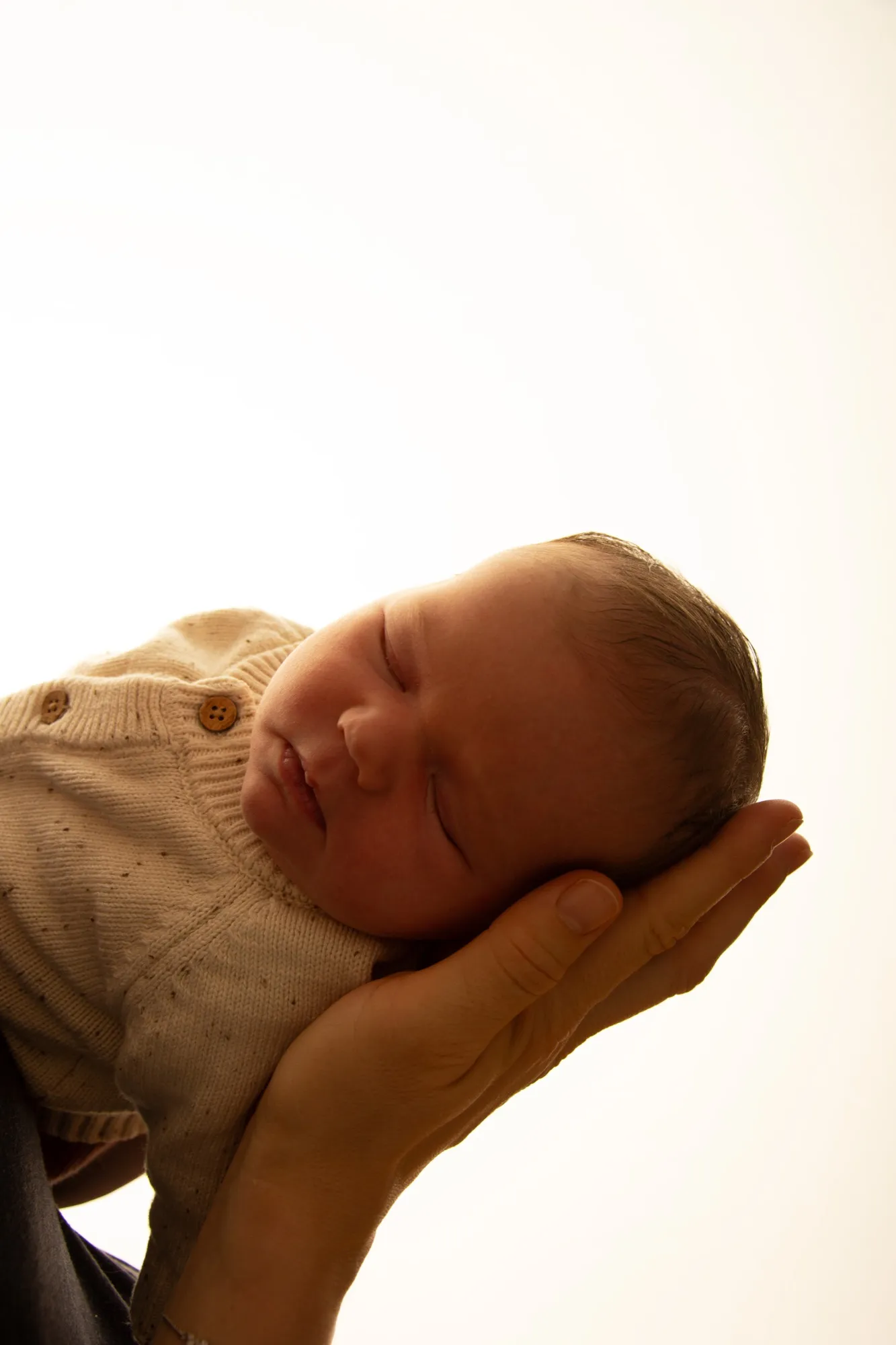 Der Kopf eines schlafenden Babys ruht in einer Hand, warmes Gegenlicht