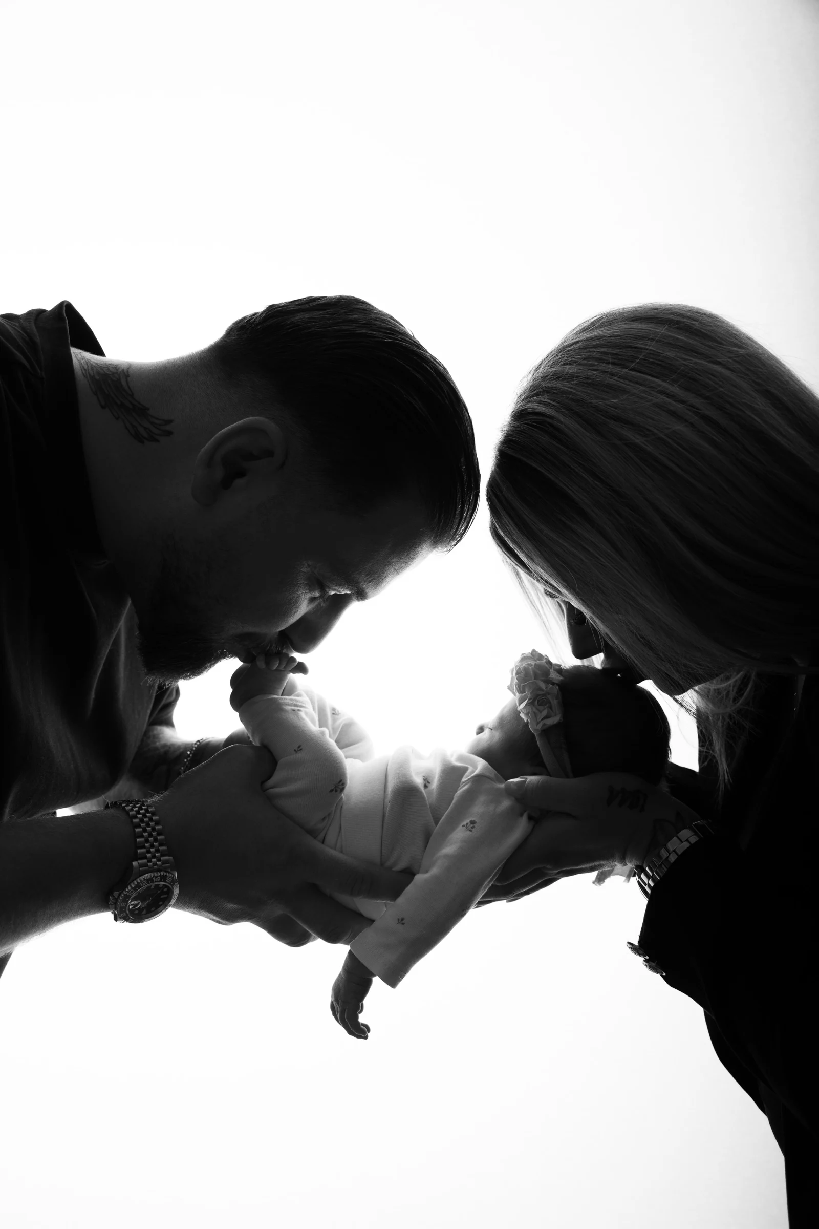 Schwarz-Weiß-Silhouette: Eltern beugen sich Stirn an Stirn über ihr Baby