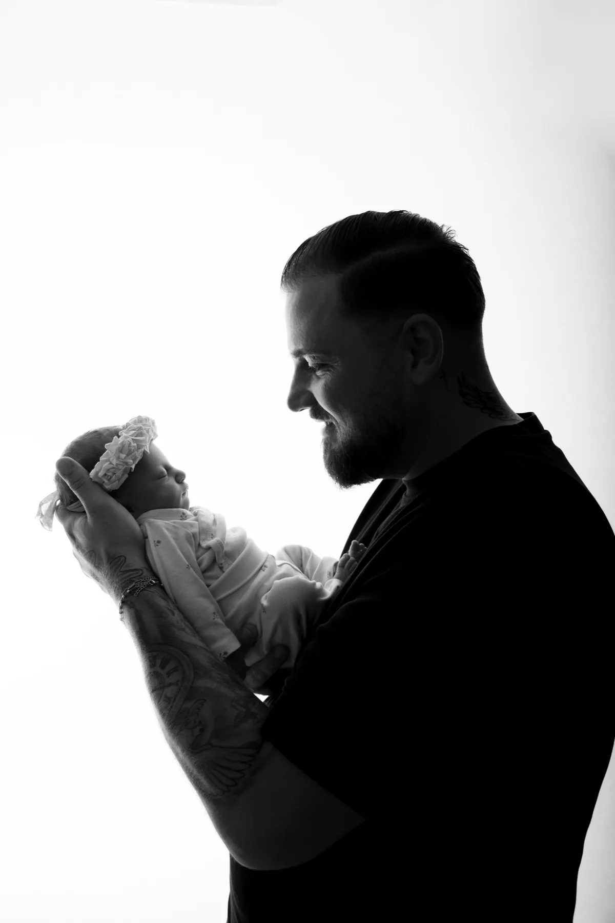 Schwarz-Weiß-Silhouette: Ein Vater hält sein Baby vor sich im Gegenlicht
